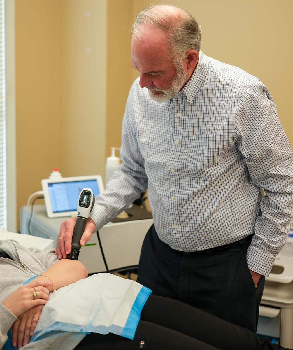 Physician applying a handheld laser therapy device to a patient's knee during a treatment session at Charleston Sports Medicine