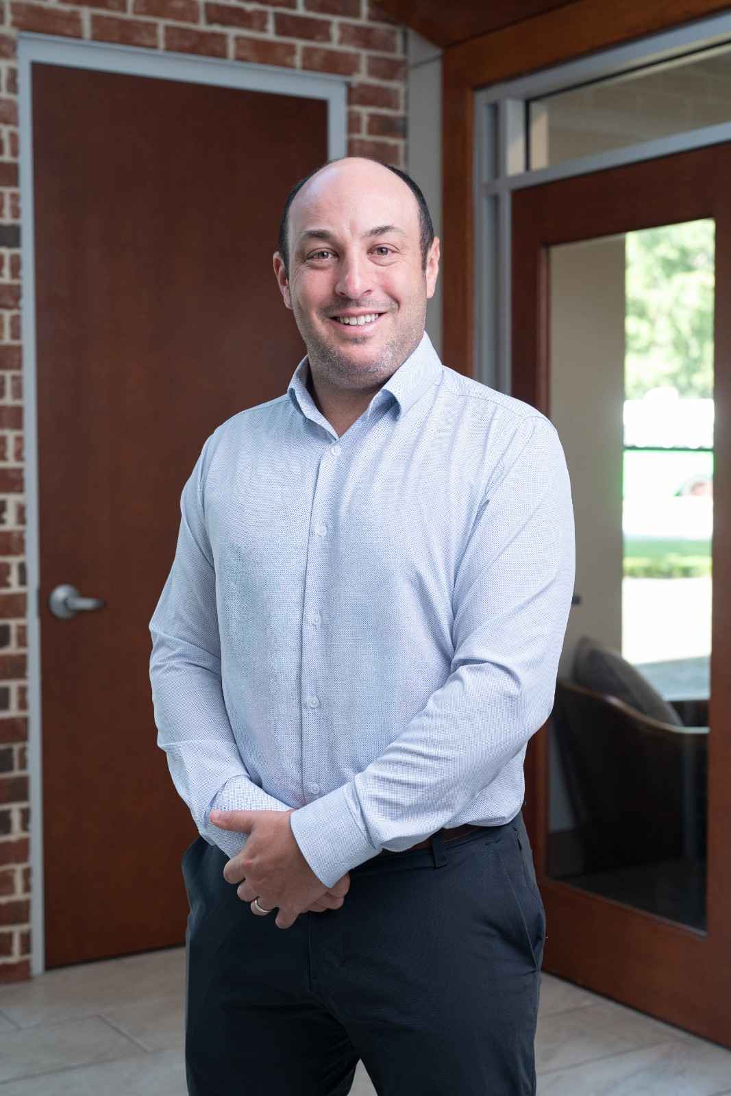 11DrFriedmanHeadshot (1) Headshot of Dr. Eric Friedman, MD, standing and smiling in a light blue dress shirt outside the Charleston Sports Medicine clinic