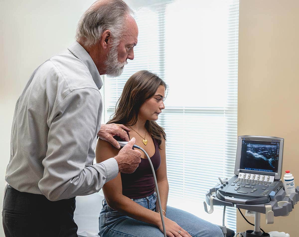 Physician performing an ultrasound-guided injection on a female patient's shoulder using a portable ultrasound machine